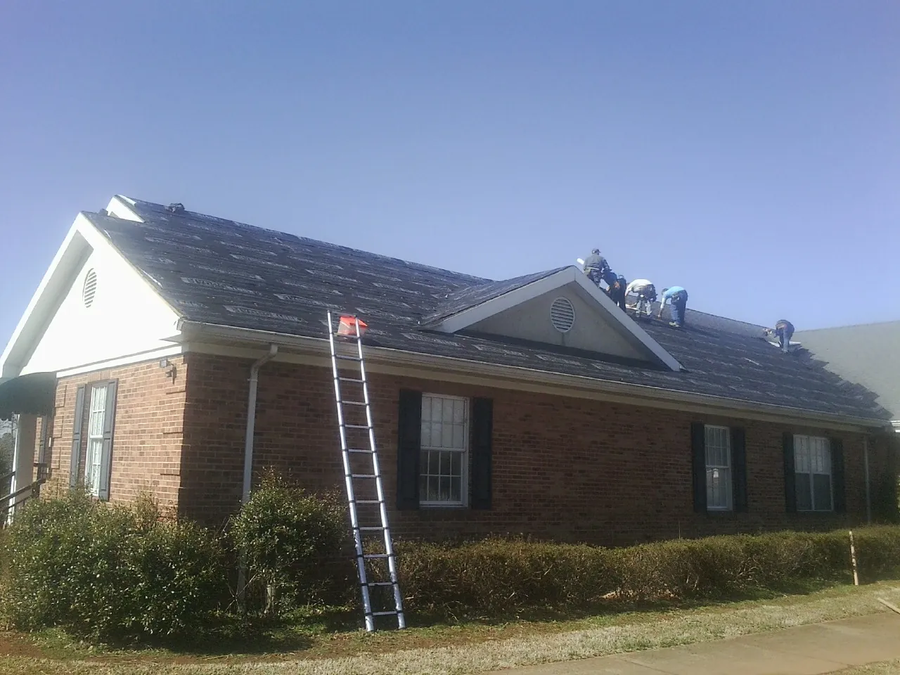 Crew tearing shingles off a brick ranch roof with a ladder set — Emergency Roof Repair work by our crew in Midway